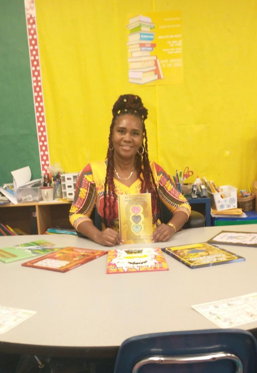 Cynthia Gadson seated at a classroom table holding one of her books